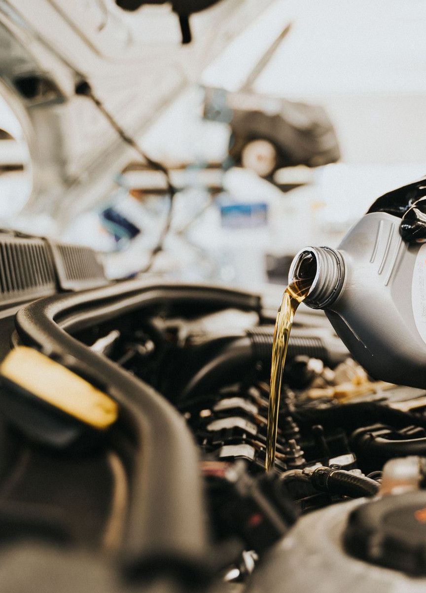 Close-up of a mechanic pouring engine oil into a car engine in an auto repair shop.